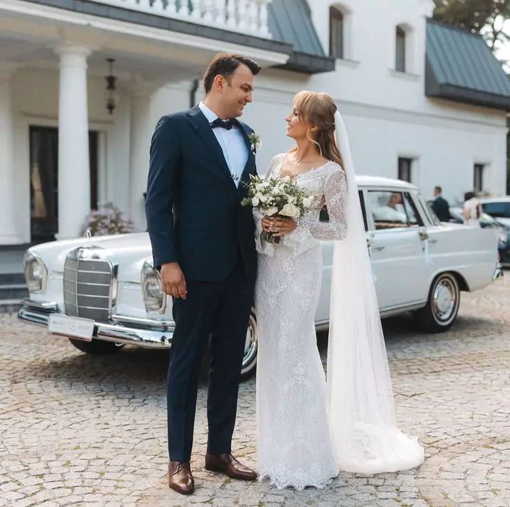 A newlywed couple standing beside a classic white Mercedes-Benz, ready for their wedding transport.